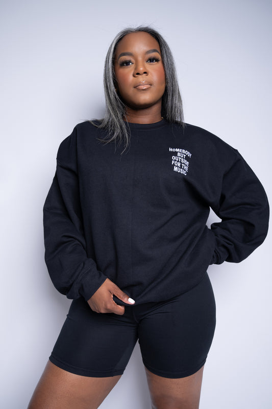 Woman wearing black embroidered sweatshirt with 'Homebody but outside for the music' stitched on the left chest