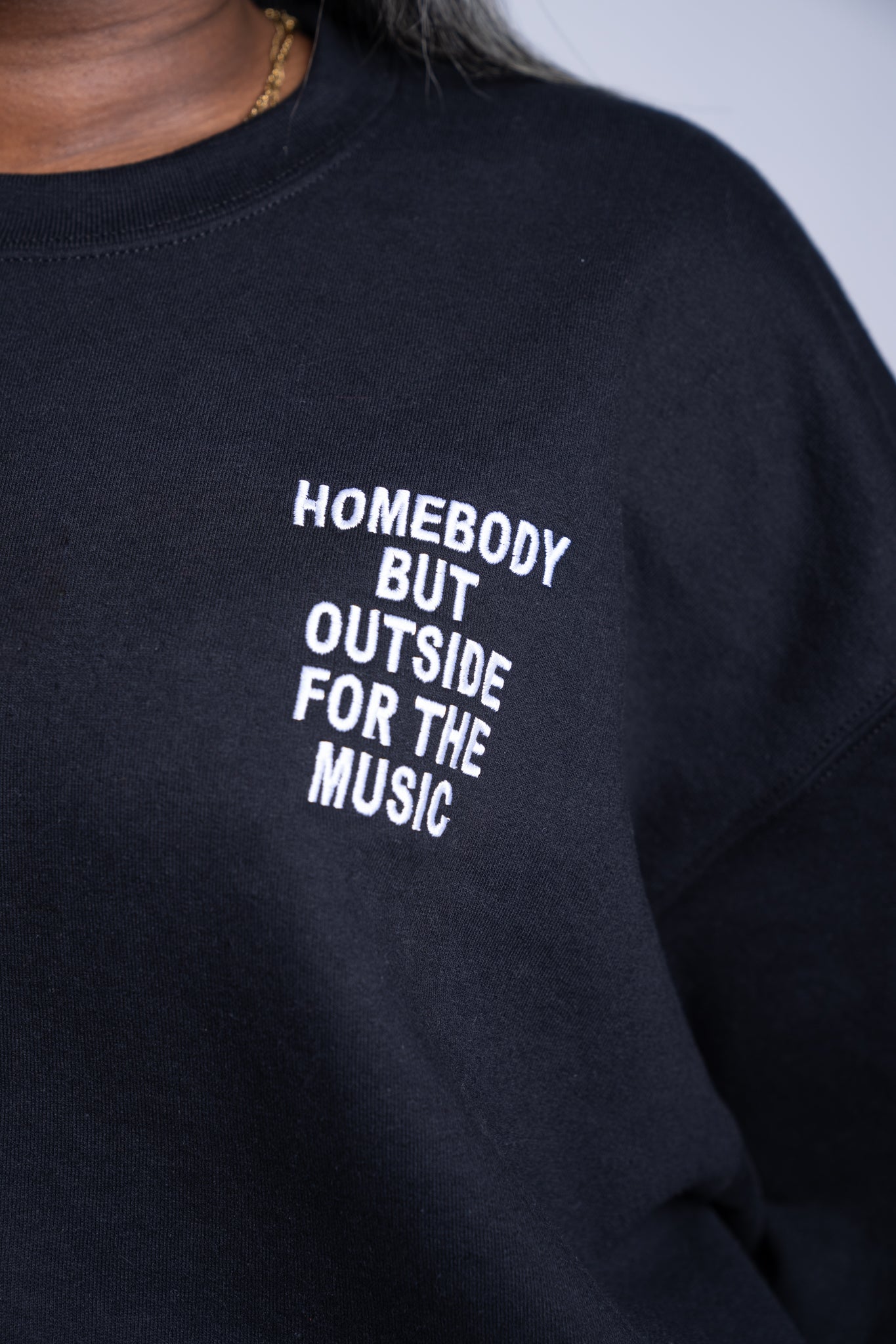 Close up of embroidery with 'Homebody but outside for the music' stitched on the left chest on a black sweatshirt